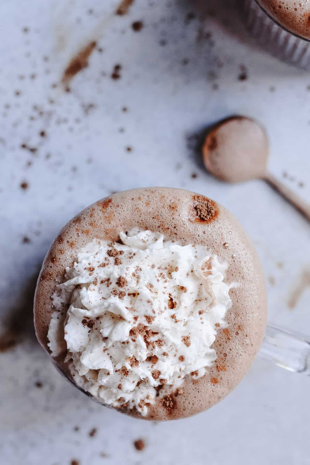 Looking down on a mug of oat milk hot chocolate with whip cream and sprinkles of unsweetened cocoa. 