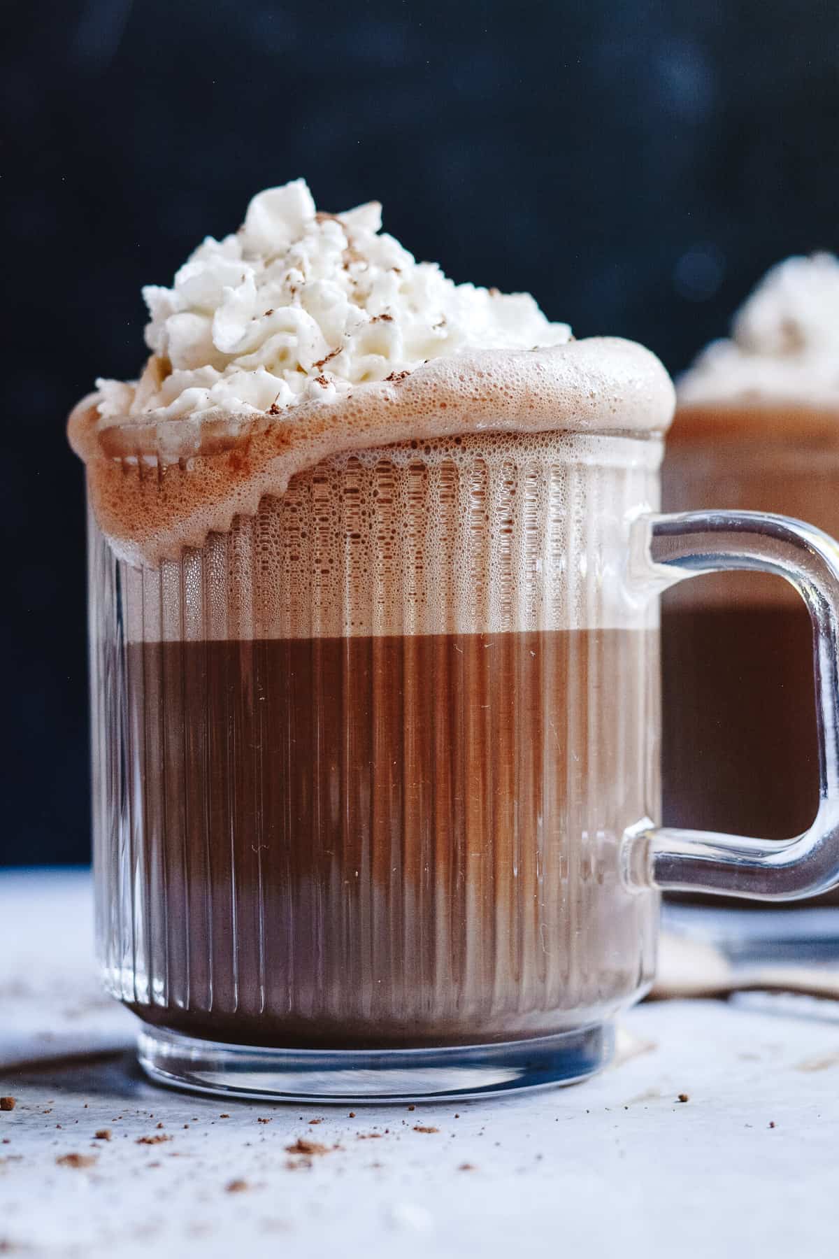 Hot chocolate in a glass mug with whip cream overflowing the edges.