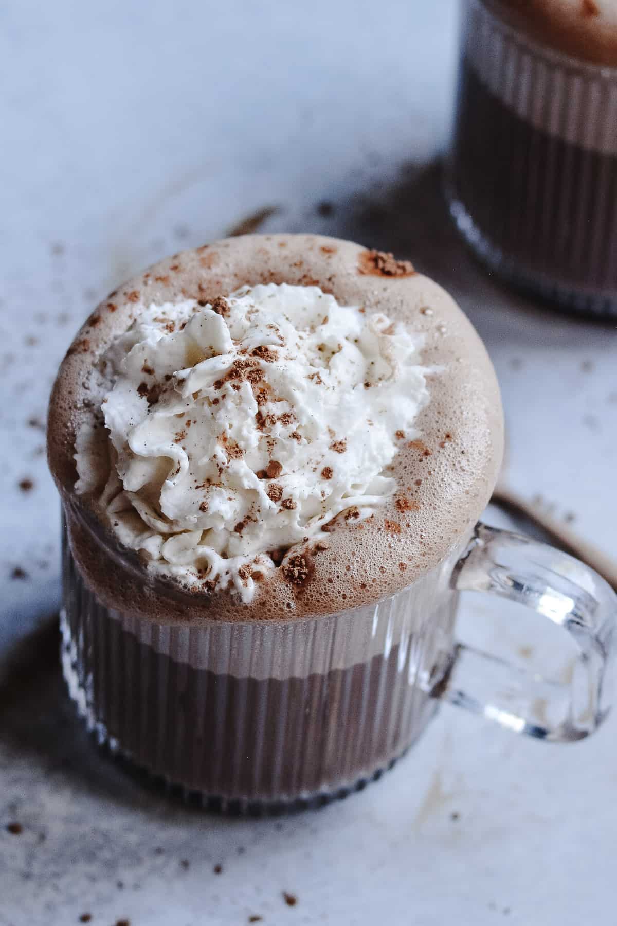 Whip cream on top of hot chocolate in a glass mug.
