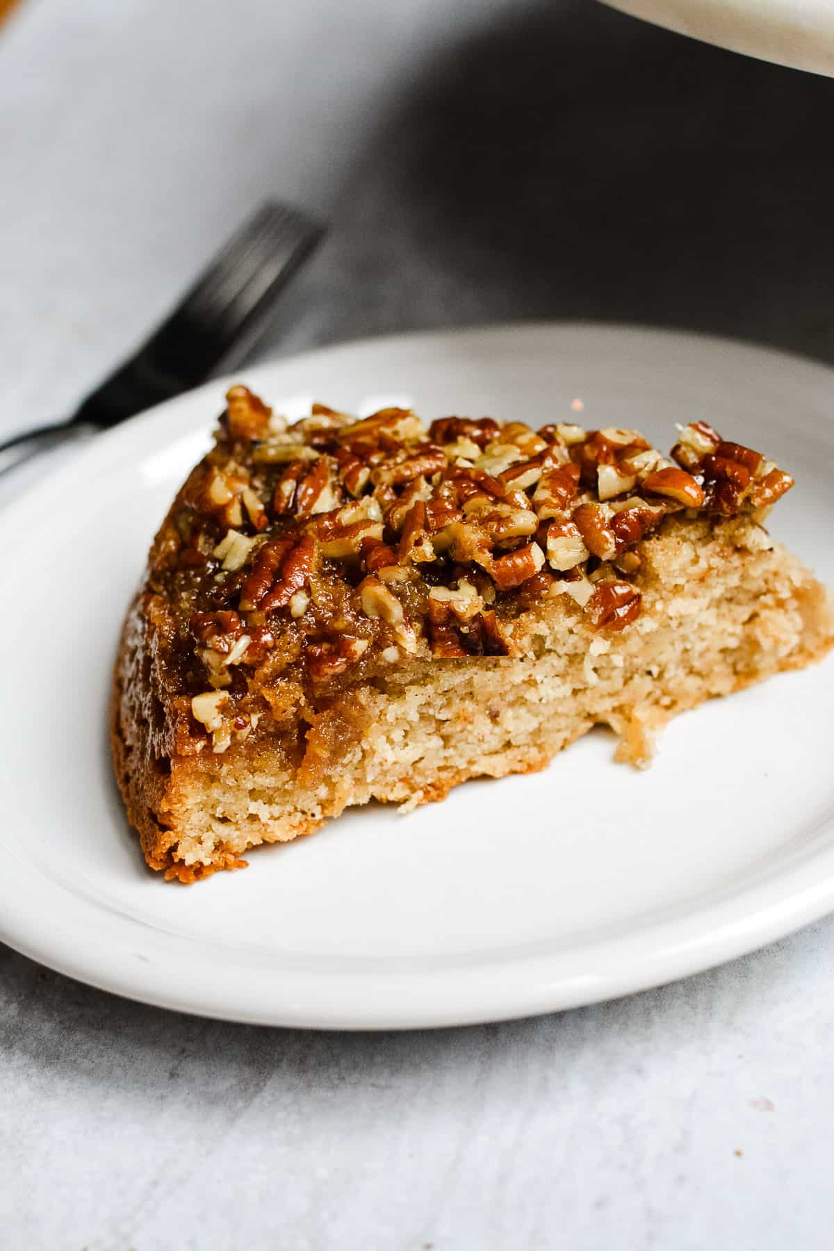 Slice of pecan upside down cake on a plate with fork in the background.