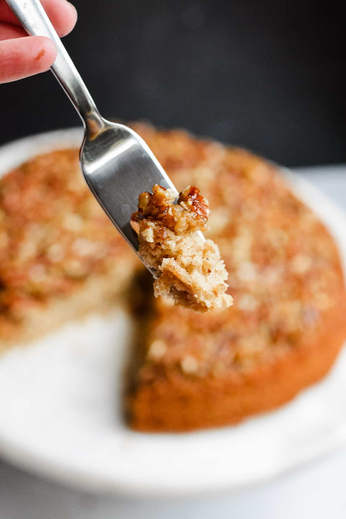 Fork with bit of pecan cake with full cake in background.