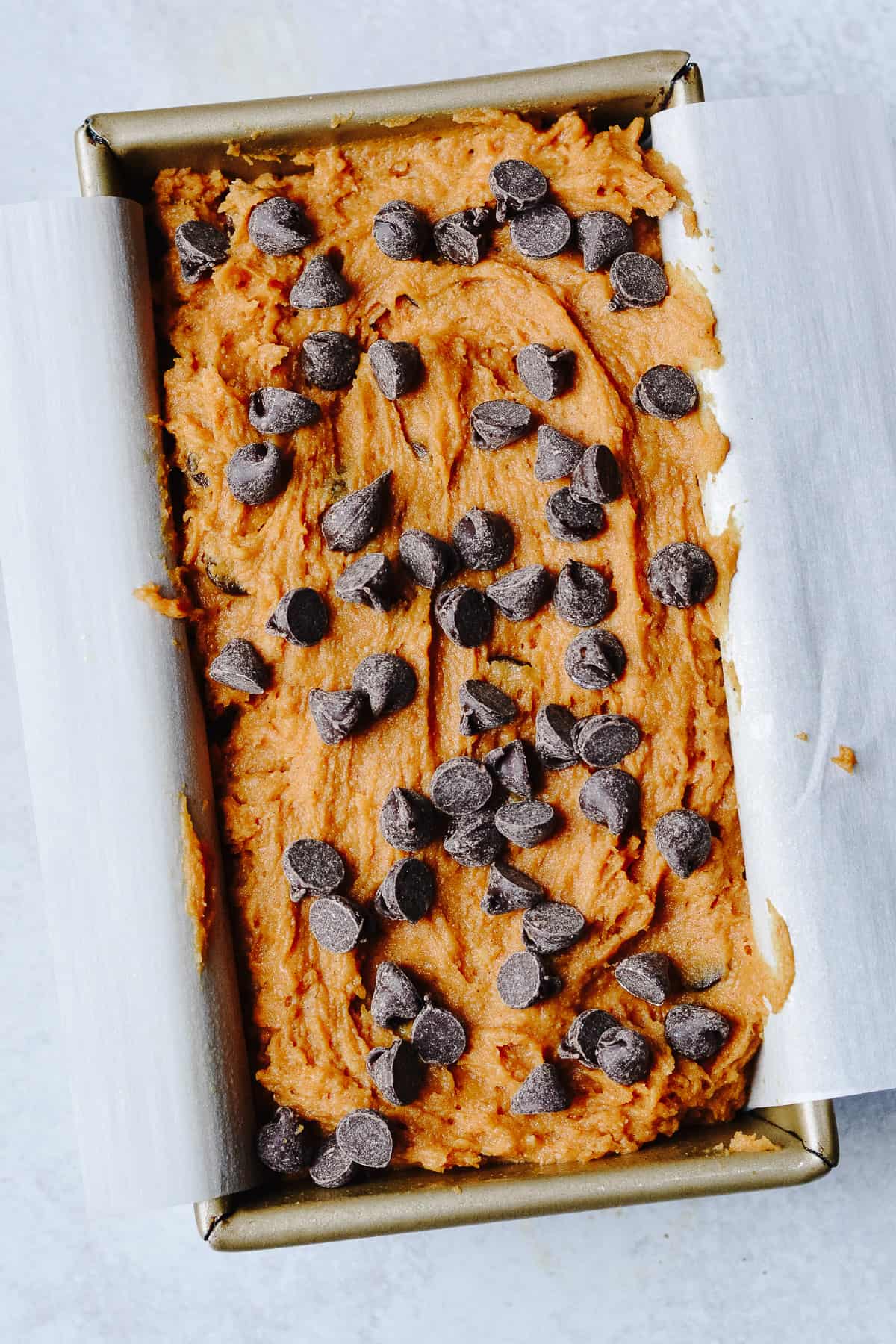 Bread batter in bread loaf pan topped with chocolate chips.