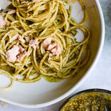Tuna pesto pasta in a bowl with bowl of pesto and parmesan.