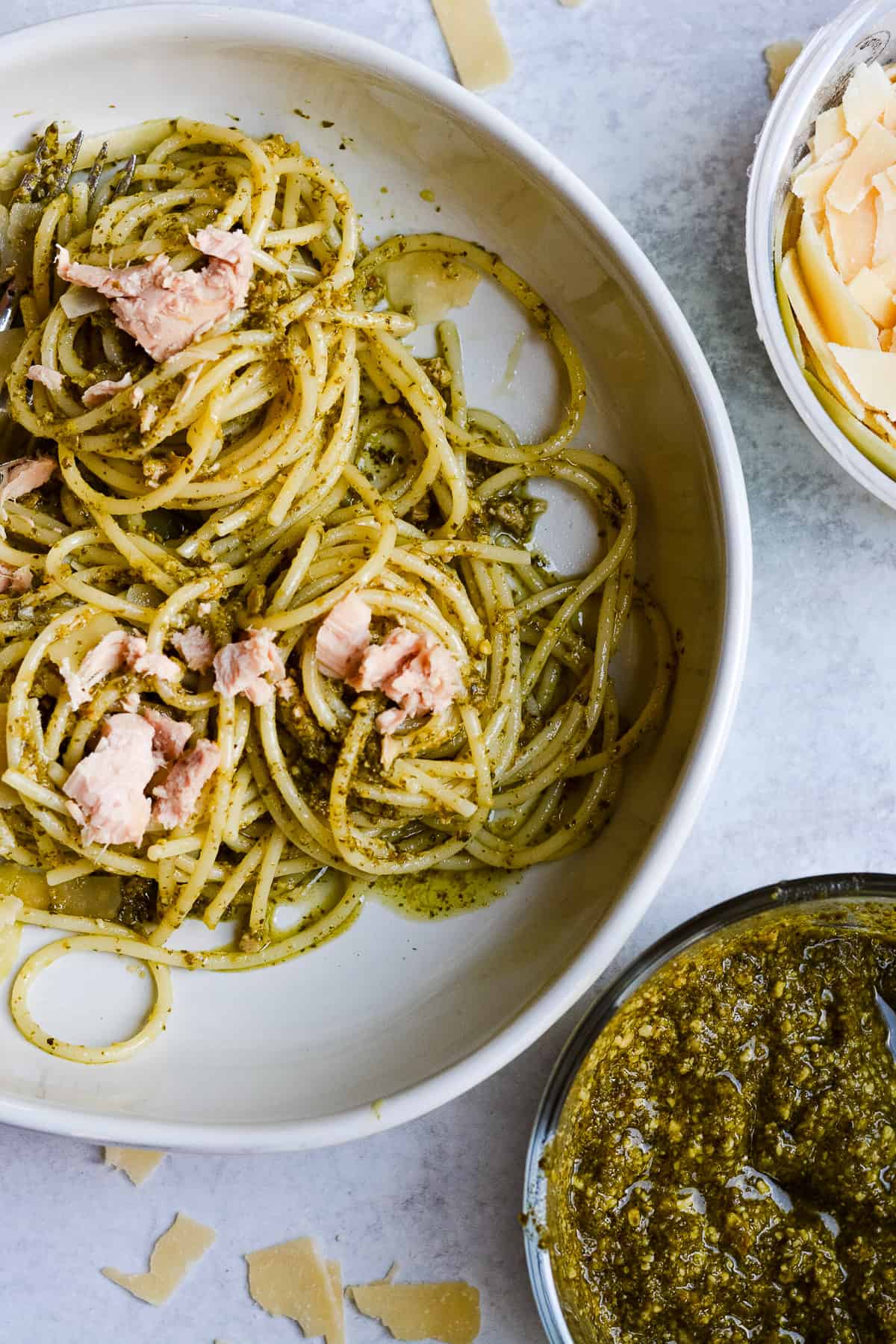 Bowl of pesto pasta with parmesan and pesto on the side.