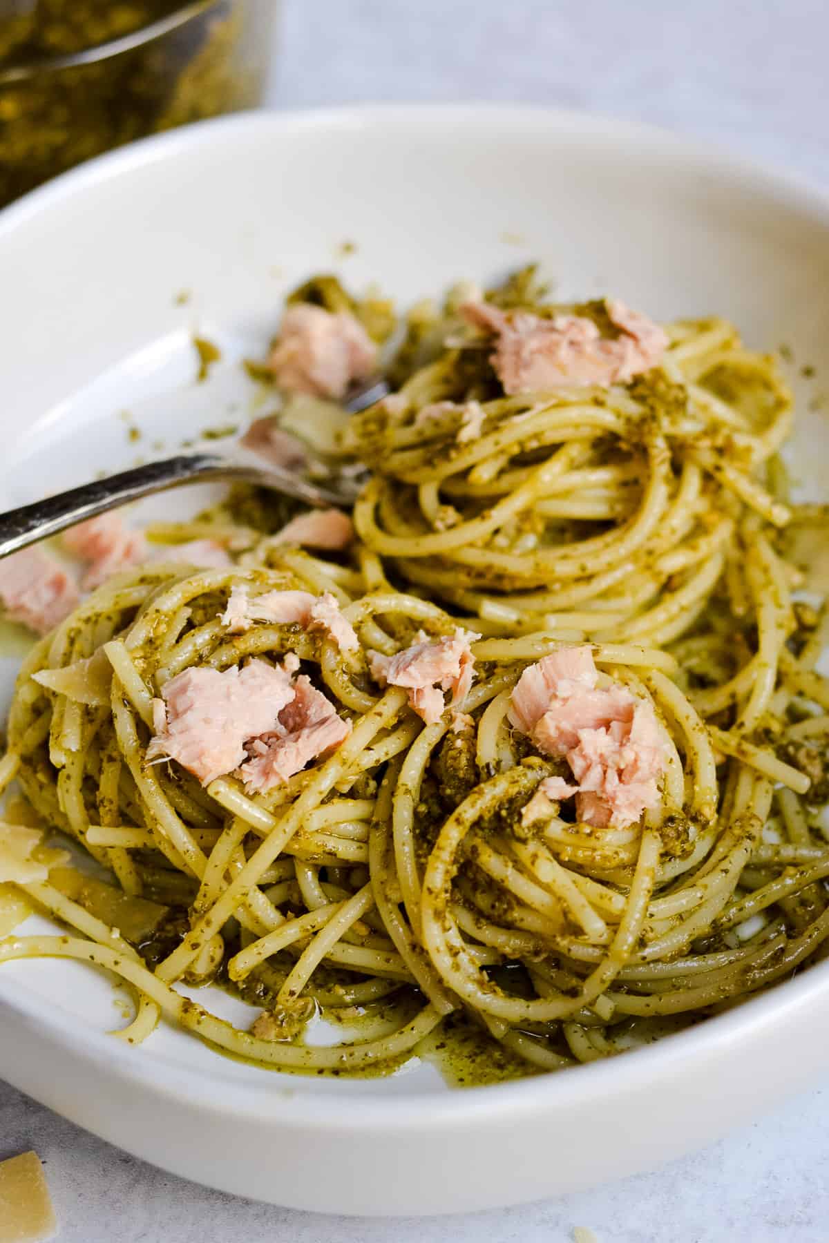 Bowl of spaghetti with pesto sauce and topped with tuna flakes.