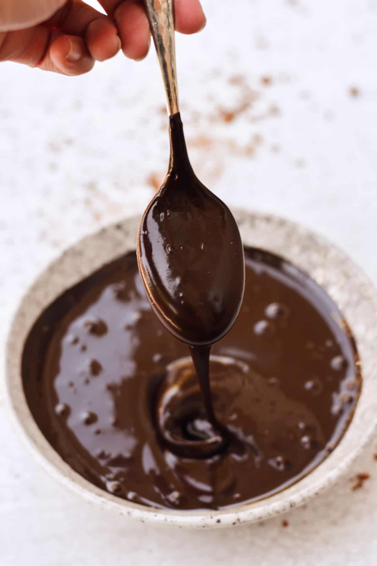 Chocolate sauce dripping off a spoon into a bowl.