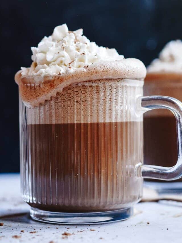 Hot chocolate in a glass mug with whip cream overflowing the edges.