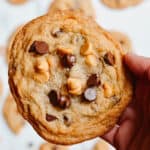 Hand holding a gluten free butterscotch chocolate chip cookie with more cookies in the background.