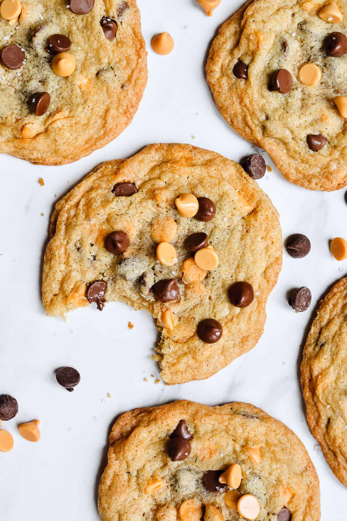 Cookies on a counter with a bite taken out of one cookie. Chocolate chips and butterscotch chips are sprinkled around.