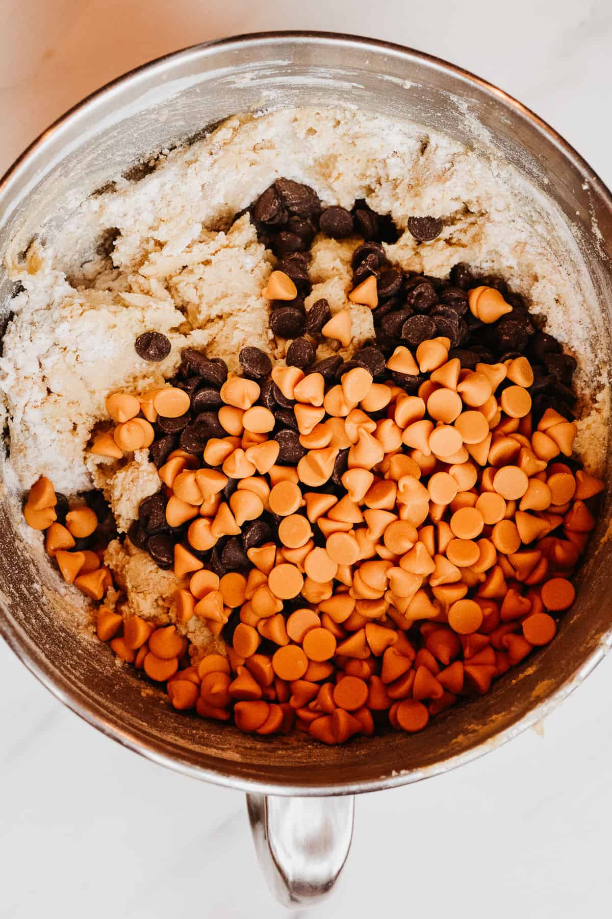 Butterscotch chips and chocolate chips on top of cookie dough ready to be mixed in.