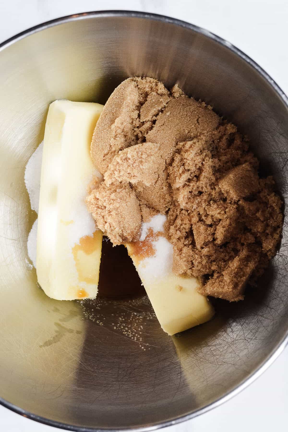 Cookie dough ingredients in mixing bowl. Butter, brown sugar, sugar and vanilla extract.