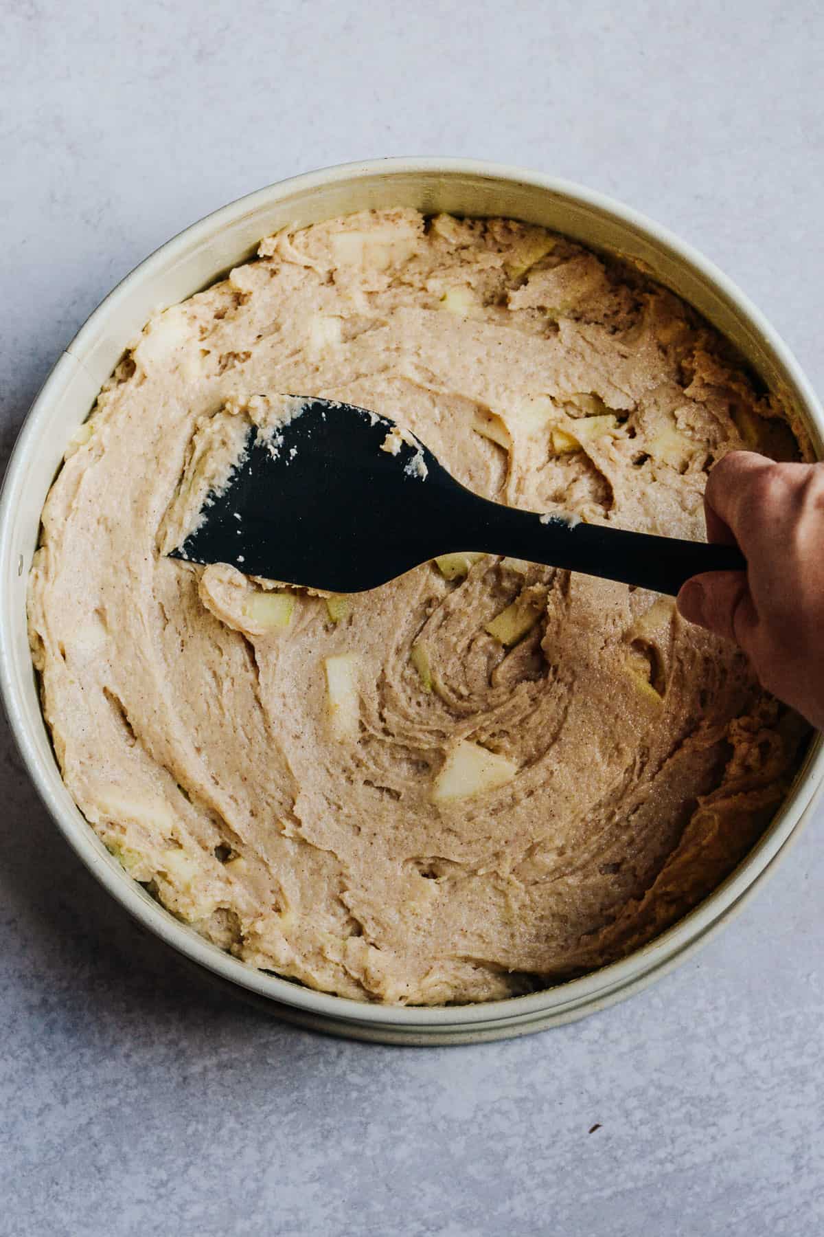 Mixed apple cake smoothed out with black spatula in spring form pan.