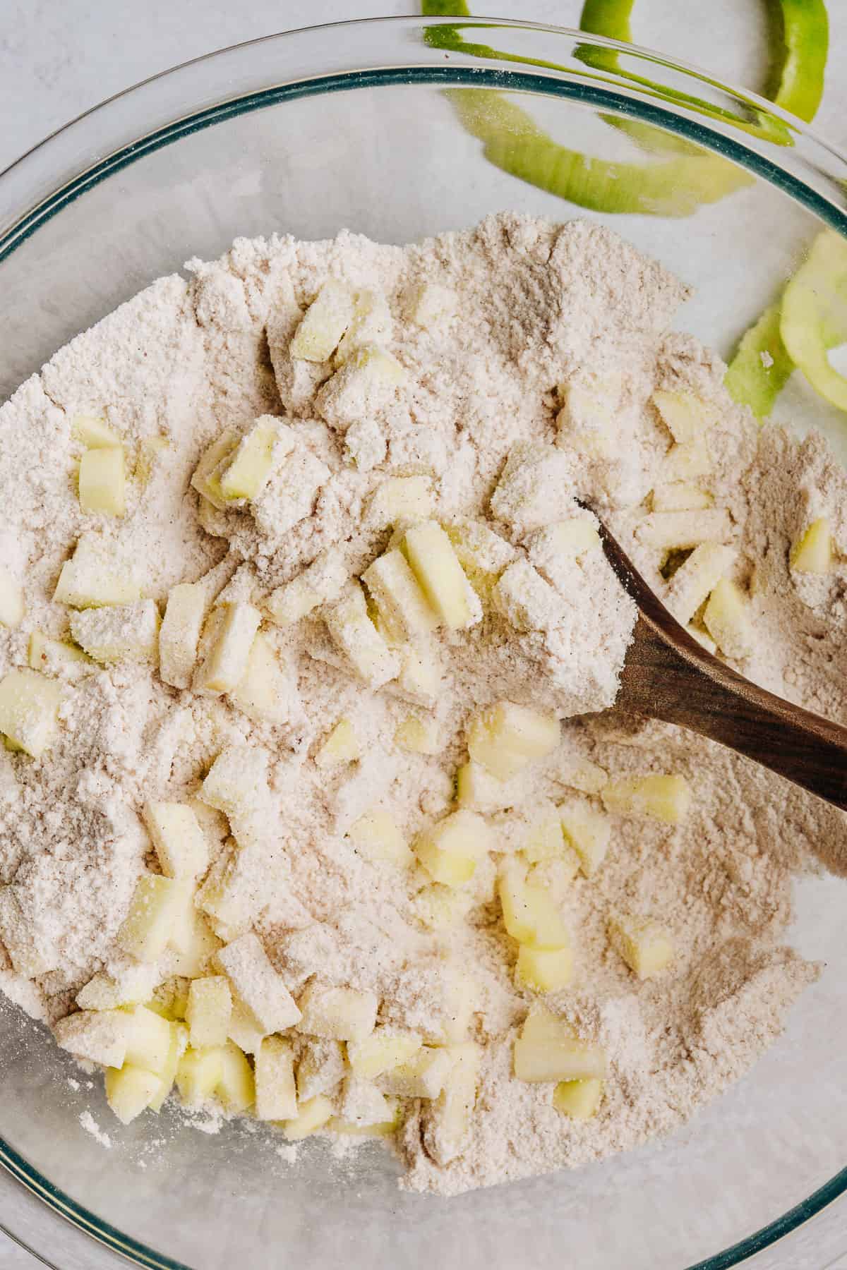 Chopped apples in flour mixture with wooden spoon.
