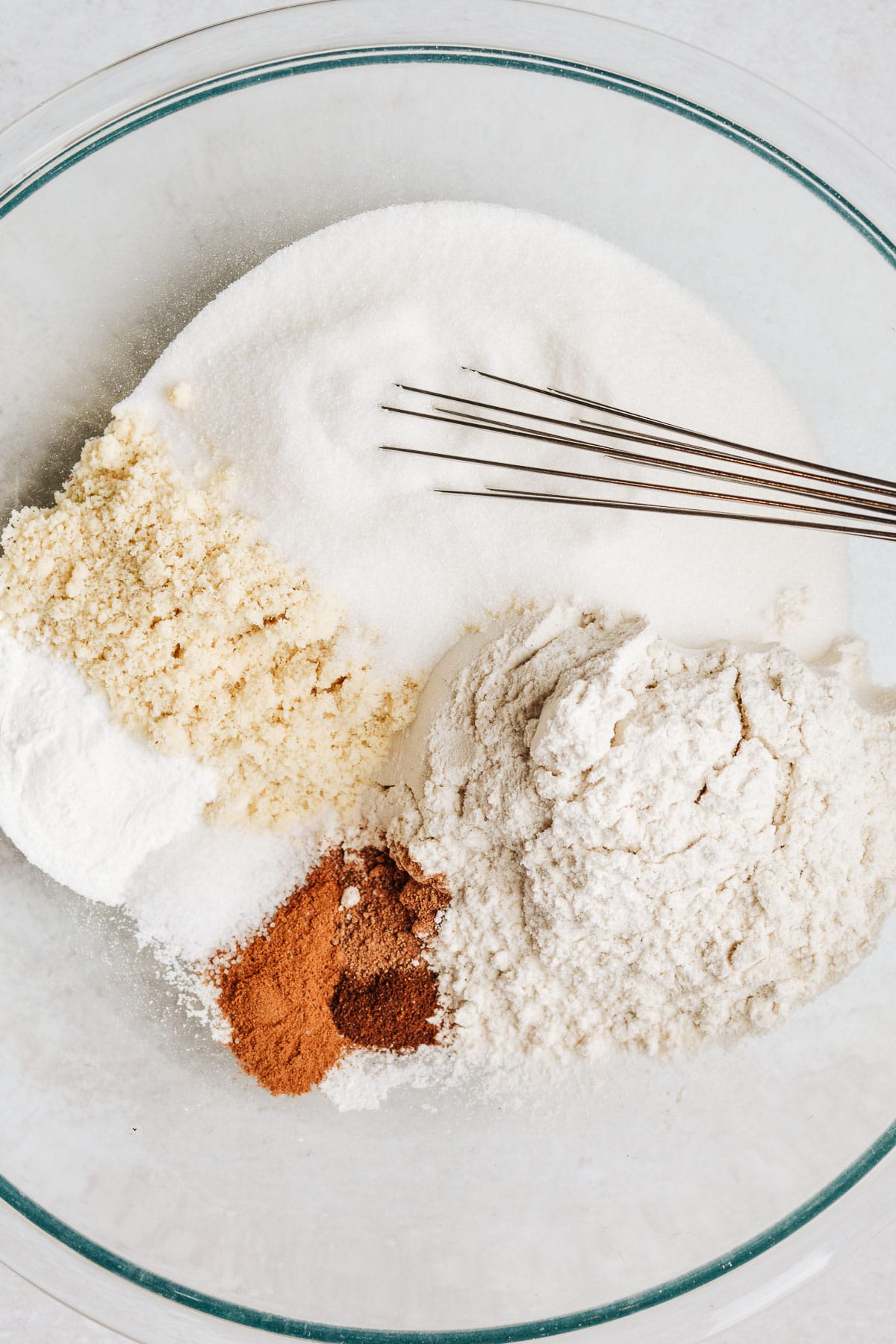 Gluten free flour, almond flour, sugar and spices in glass bowl with whisk.