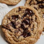 Close up of maple chocolate chunk cookie with melted chips and more cookies behind.