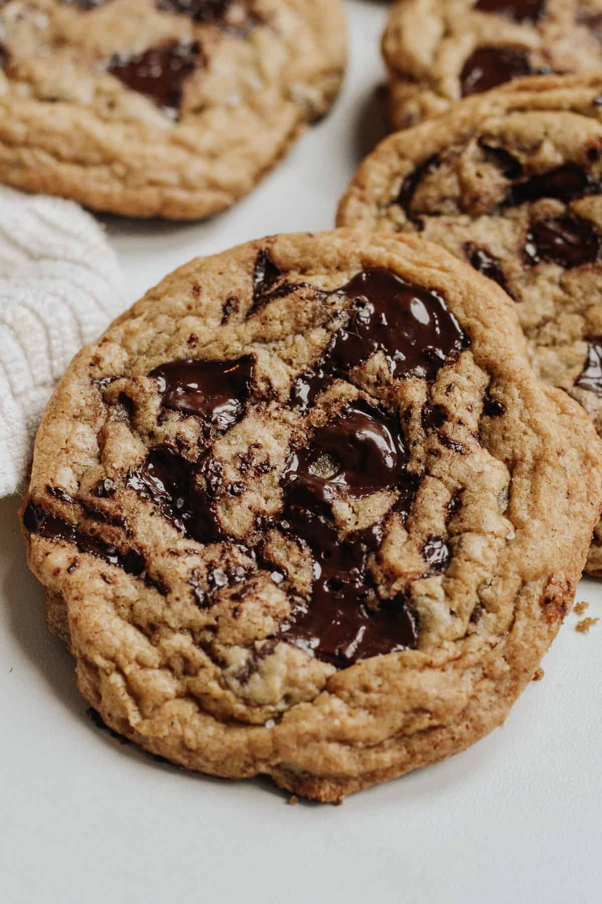 Close up of maple chocolate chunk cookie with melted chips and more cookies behind.