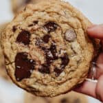 Hand holding maple chocolate chip cookies with melted chunks and sprinkled with se salt.