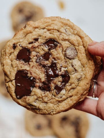 Hand holding maple chocolate chip cookies with melted chunks and sprinkled with se salt.