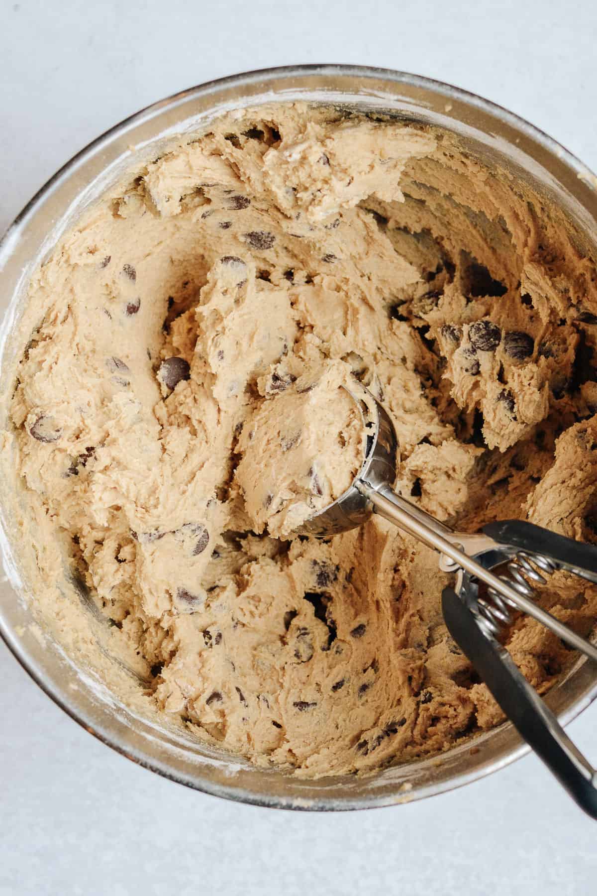 Cookie dough in a mixing bowl with a cookie scoop.
